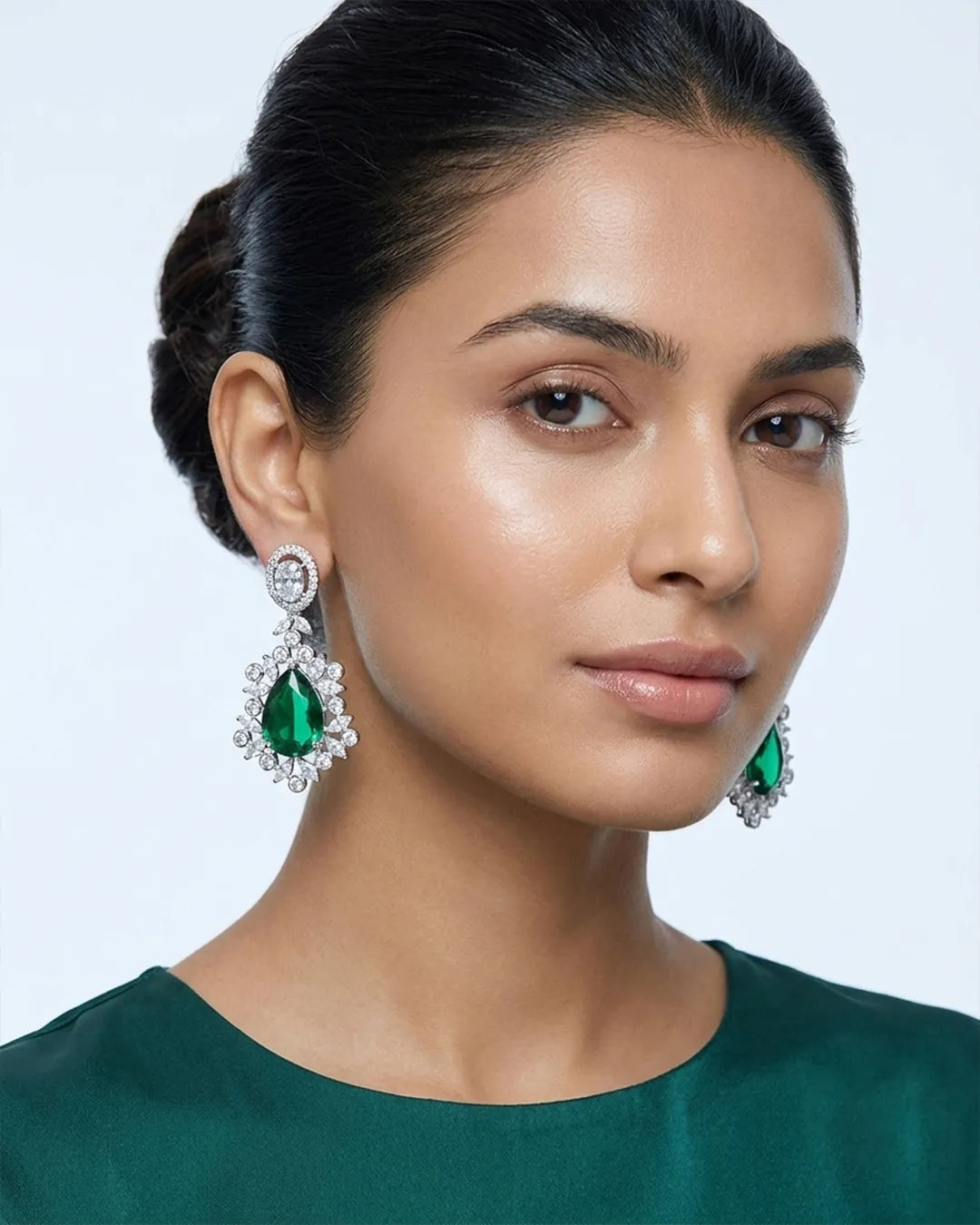 Woman wearing emerald green earrings with a plain background