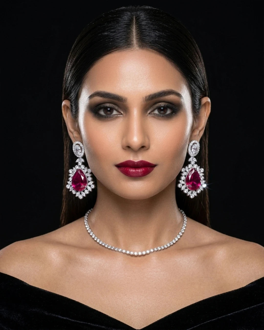 Woman wearing red gemstone earrings and a pearl necklace against a black background