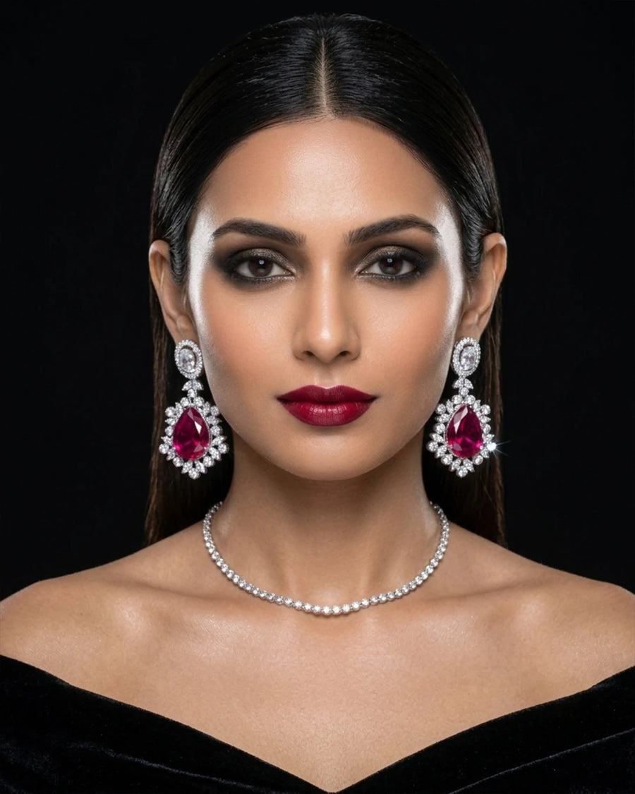 Woman wearing red gemstone earrings and a pearl necklace against a black background