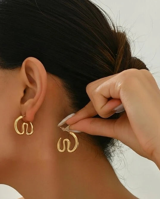 Gold hoop earrings being worn and adjusted by a hand against a neutral background
