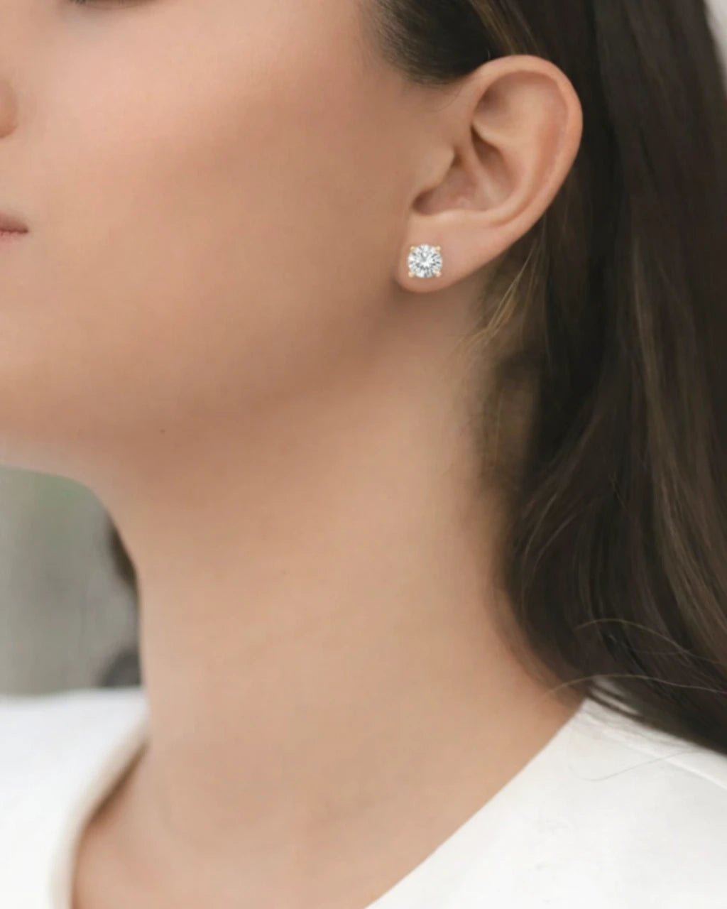Close-up of a person wearing diamond stud earrings with a blurred background