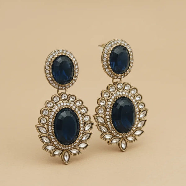 Pair of ornate earrings with dark blue gemstones and gold detailing on a beige background