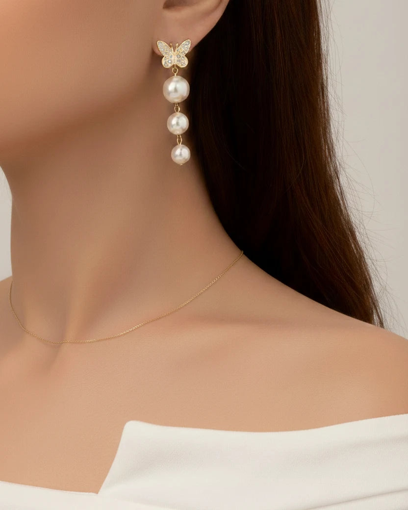 Pearl earrings with butterfly detail worn by a model against a neutral background