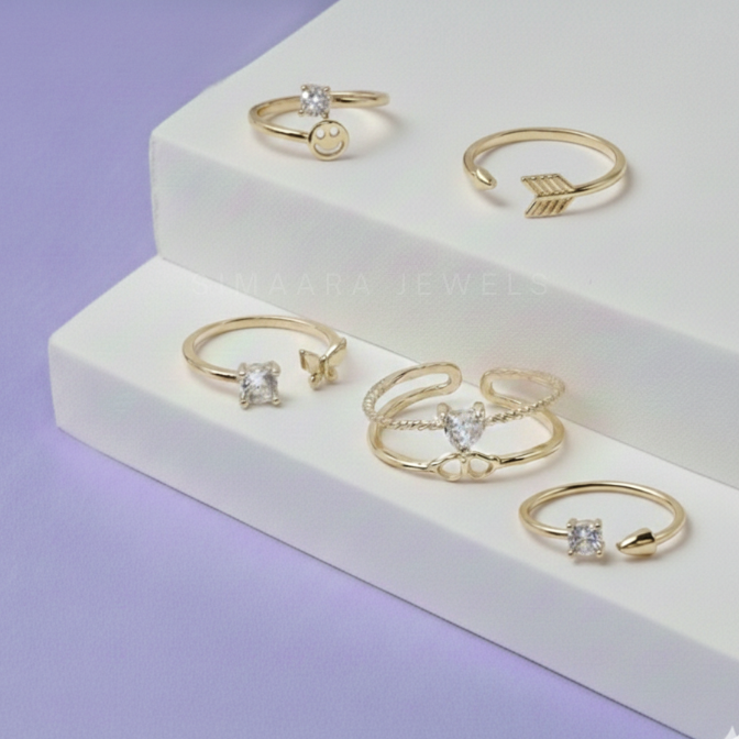 Set of gold rings with gemstones on a white platform against a purple background