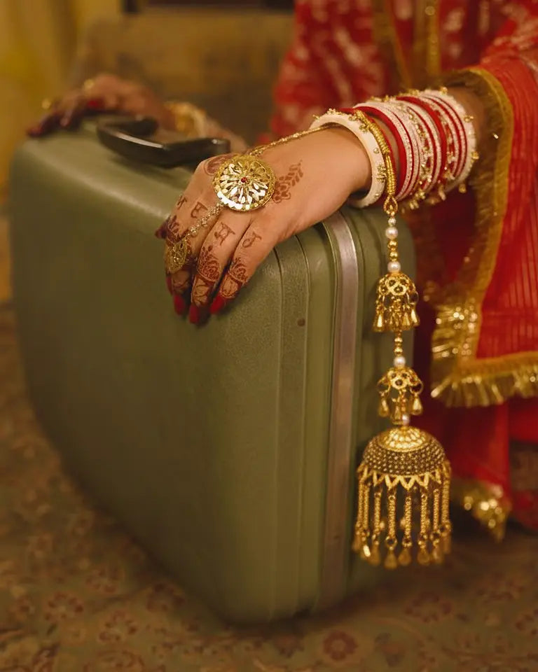 Person with gold jewelry holding a suitcase, wearing a red and gold traditional outfit.