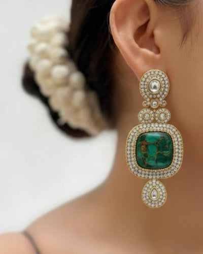 Close-up of a person wearing an ornate earring with a green gemstone.