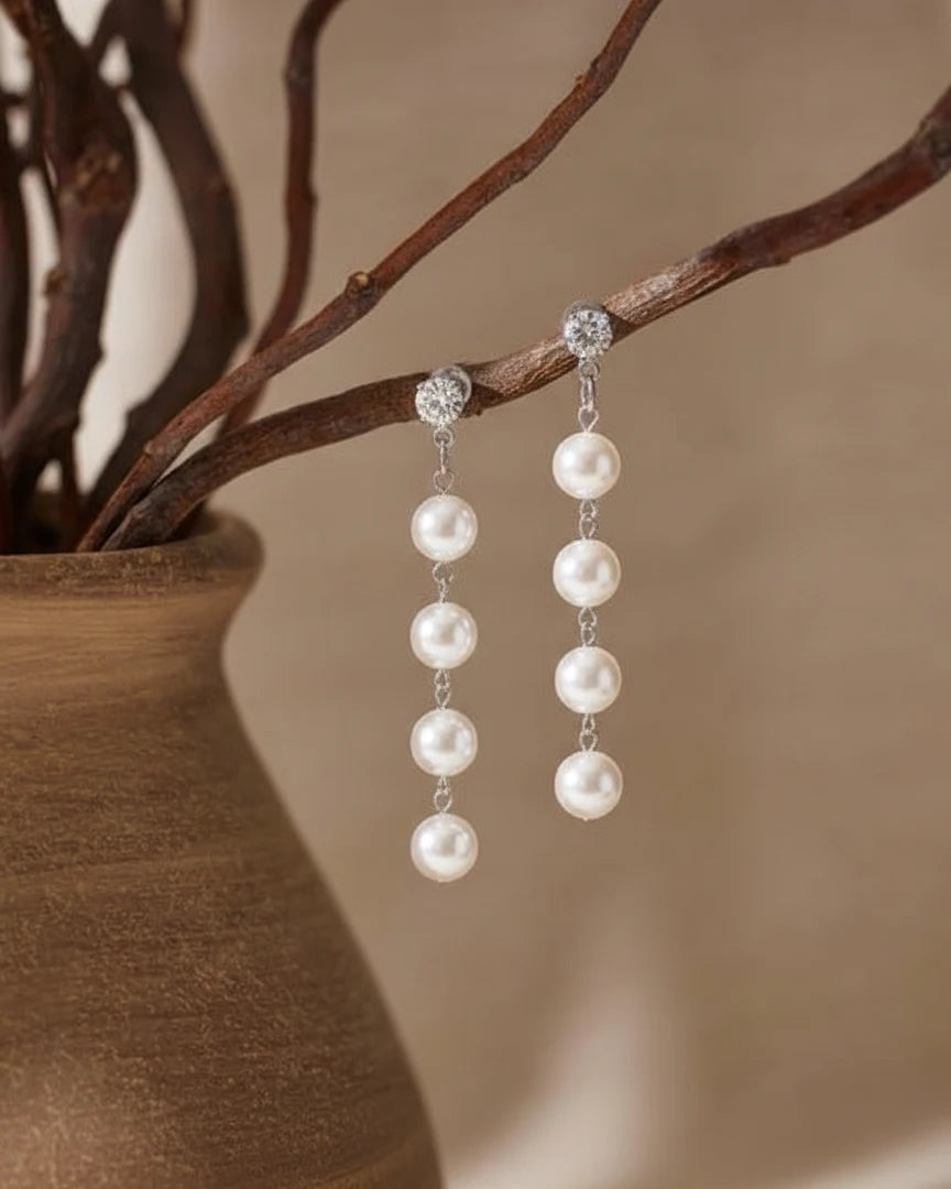 Pearl earrings hanging from a branch with a neutral background