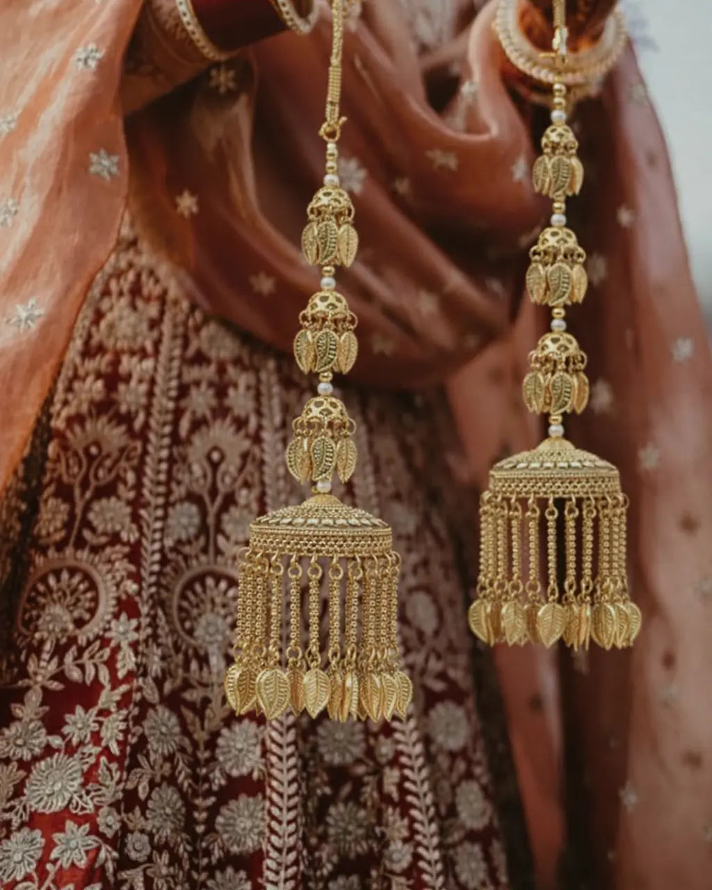 Gold jhumka earrings held in front of a patterned fabric background