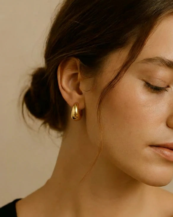 Close-up of a person wearing gold hoop earrings with a neutral background