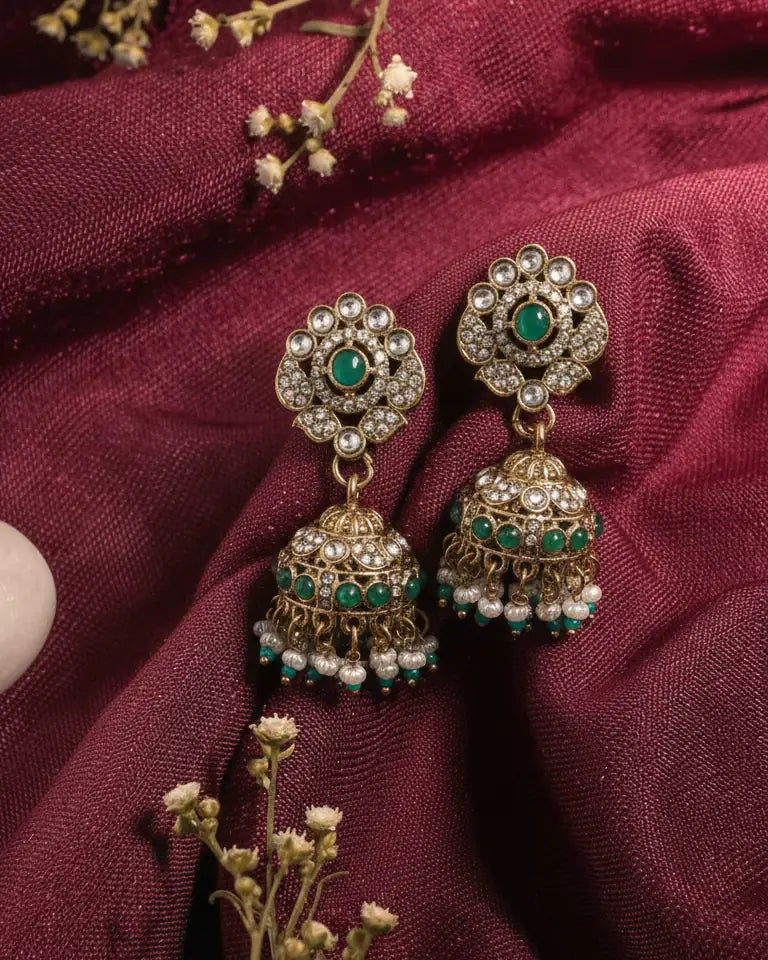 Ornate earrings with green gemstones on a maroon fabric background
