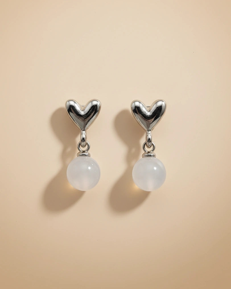 Heart-shaped earrings with white beads on a beige background