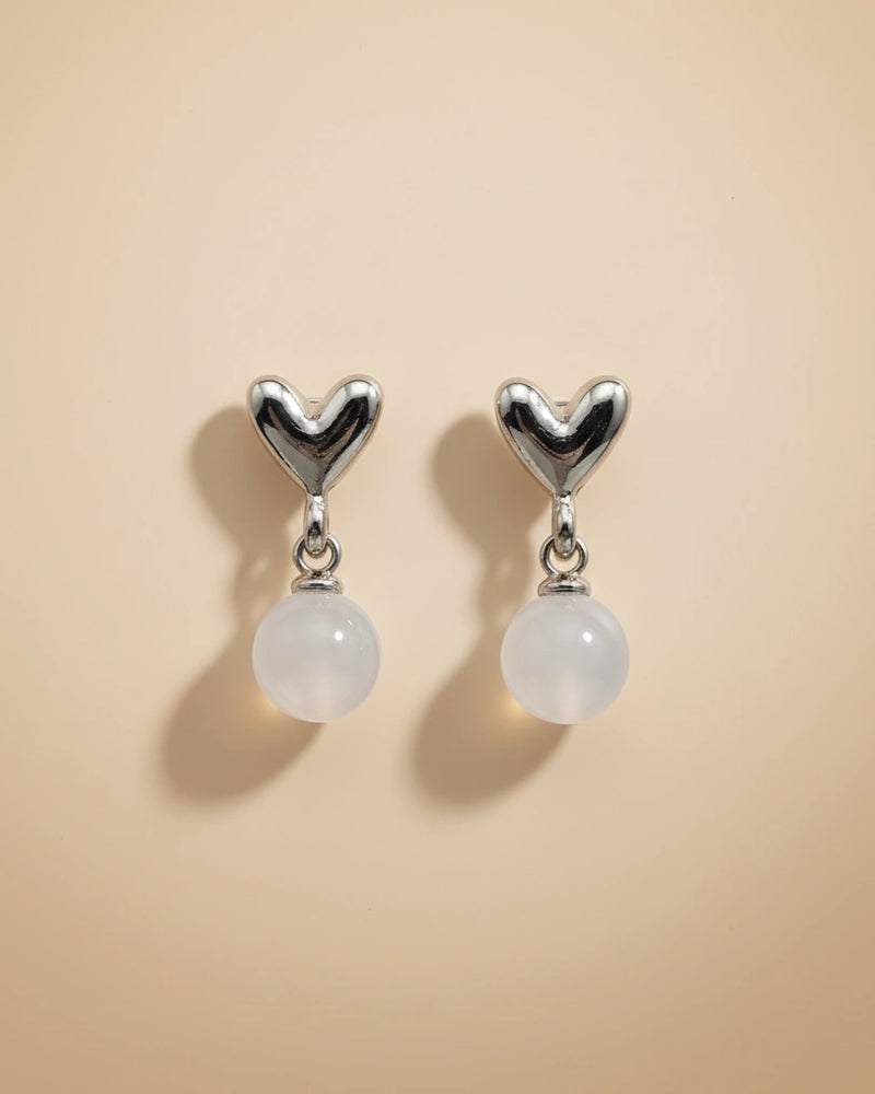 Heart-shaped earrings with white beads on a beige background