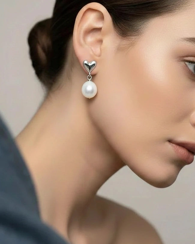 Pearl earring with heart charm worn by a model against a neutral background