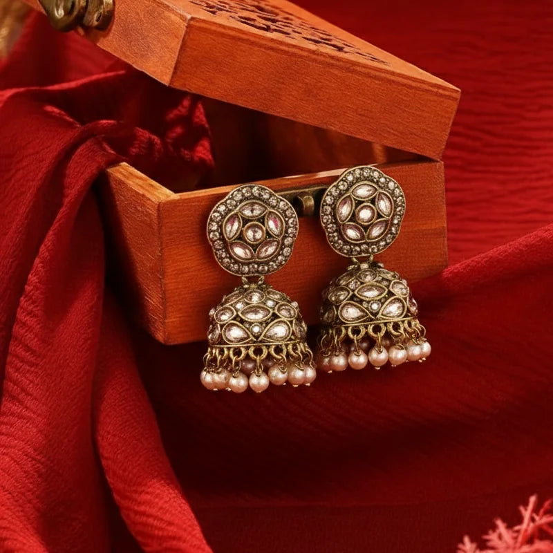 Ornate earrings with pearl details in a wooden box on a red fabric background