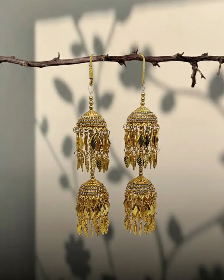 Gold earrings hanging from a branch with a neutral background