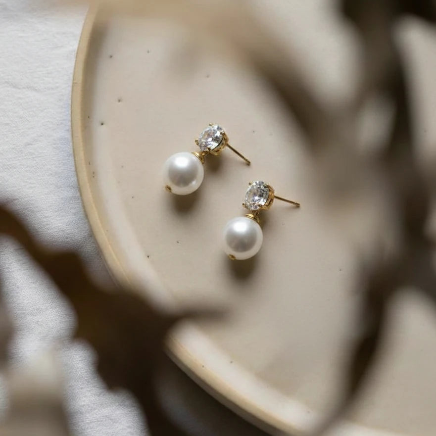 Pearl and crystal stud earrings on a beige ceramic dish.