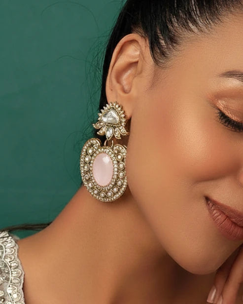 Close-up of a woman wearing ornate earrings with a teal background