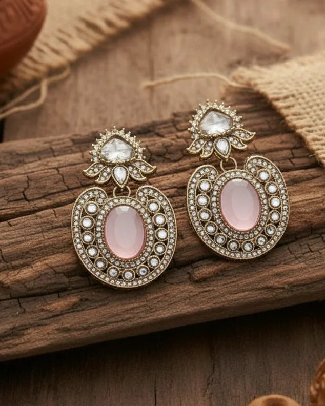 Ornate earrings with pink stones on a wooden surface