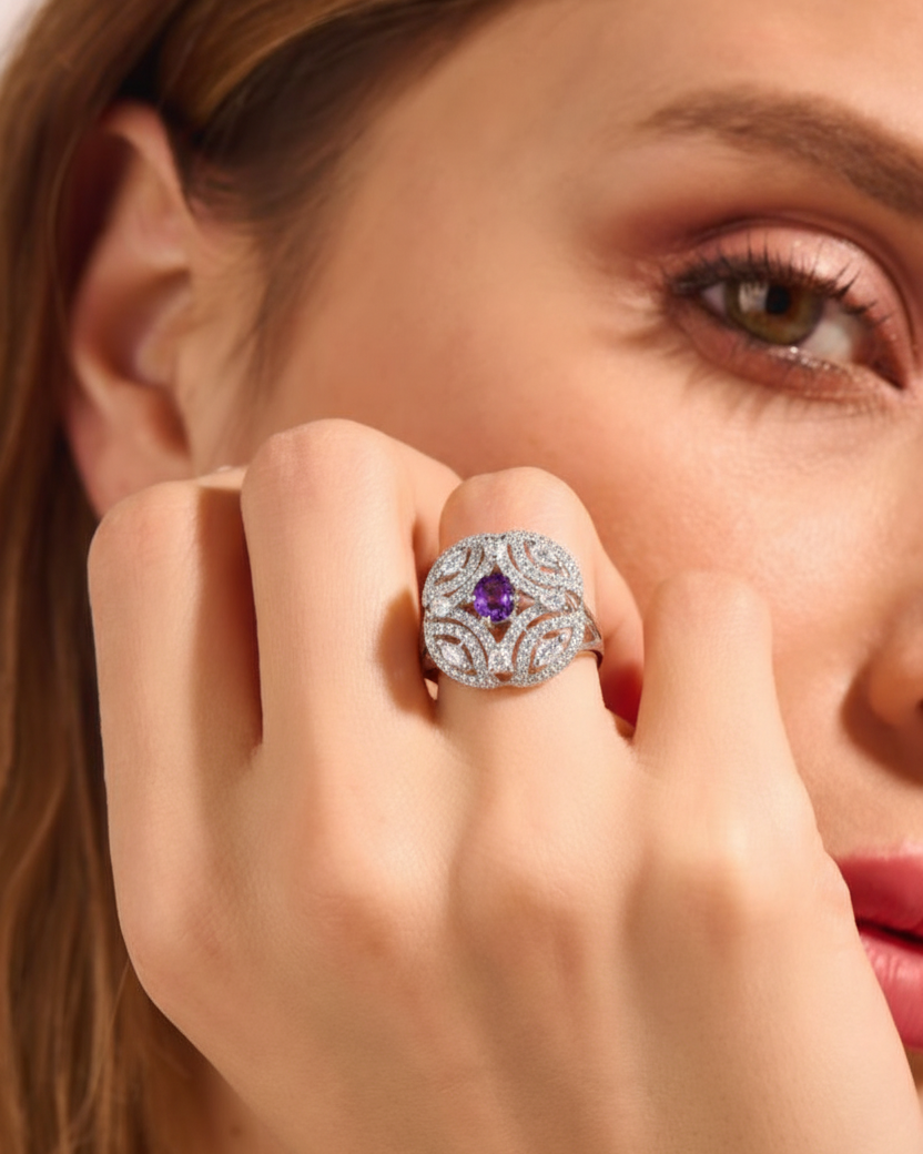 Close-up of a woman's hand wearing an ornate ring with a purple gemstone, touching her face.