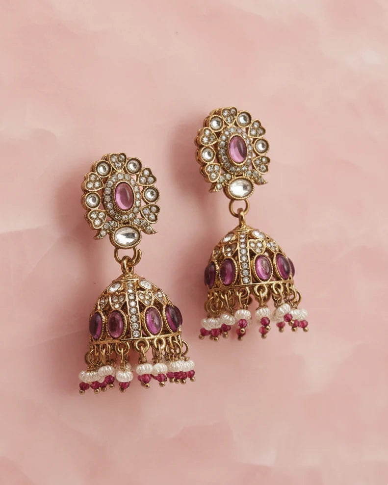Ornate earrings with pink and purple stones on a pink background