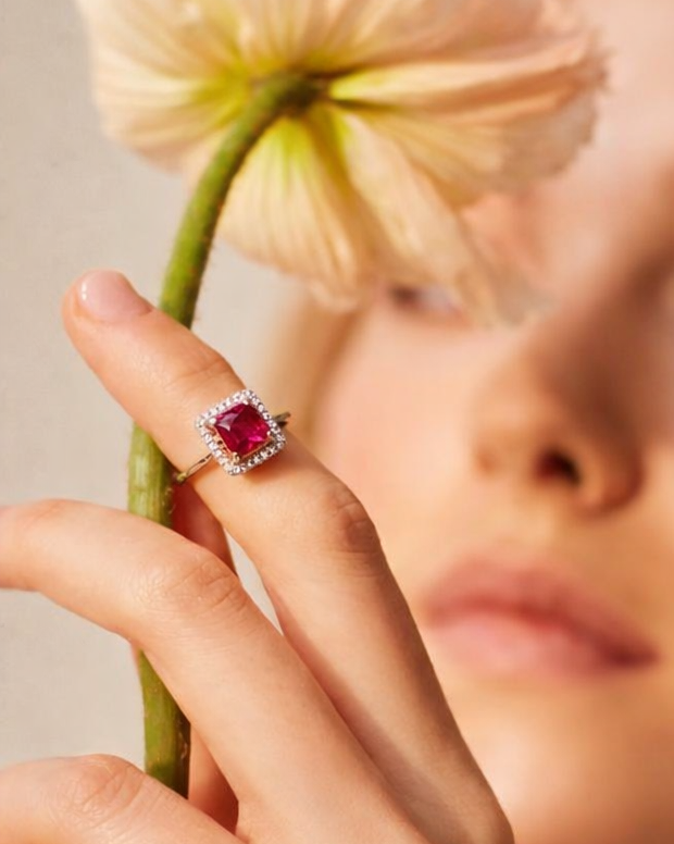 Close-up of a hand wearing a ring with a red gemstone, holding a flower.