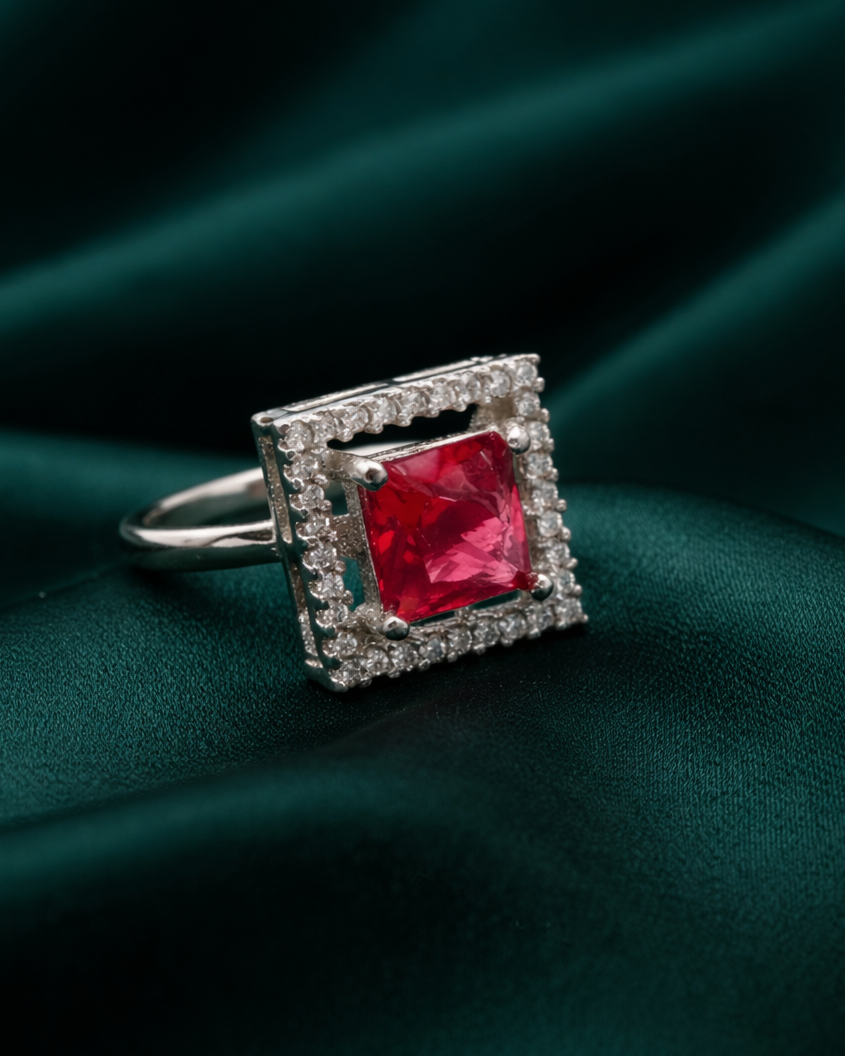 Ring with a red gemstone and diamond-studded square halo on a dark green fabric background