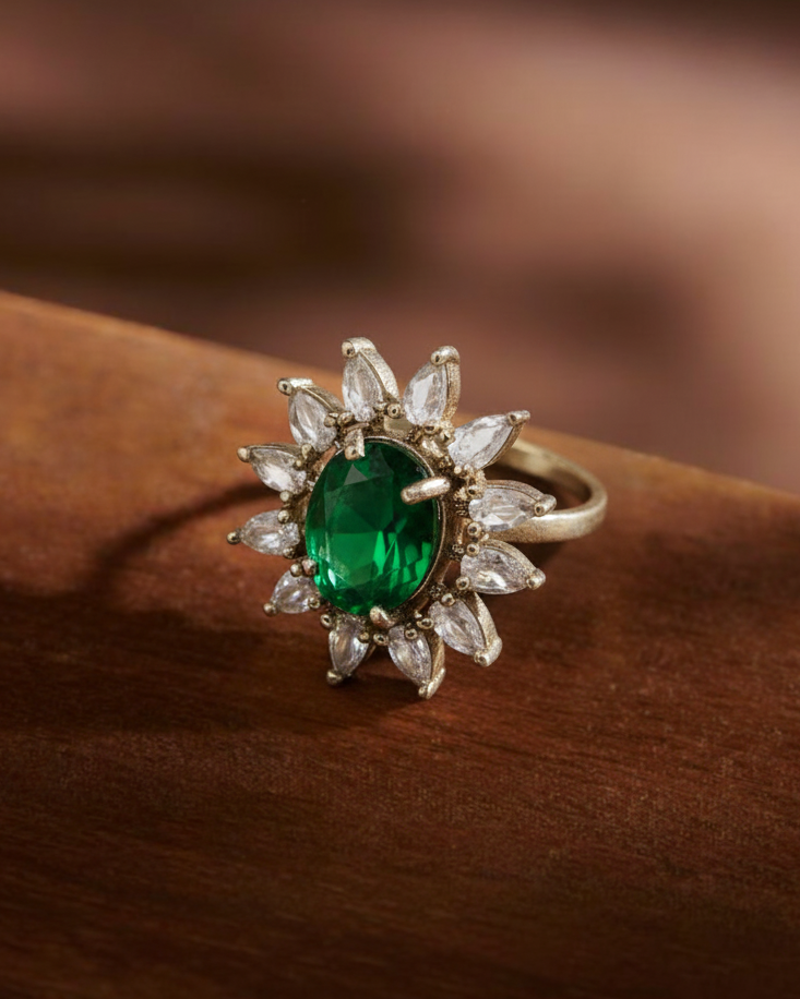 Gold ring with a green gemstone and diamond-like stones on a wooden surface