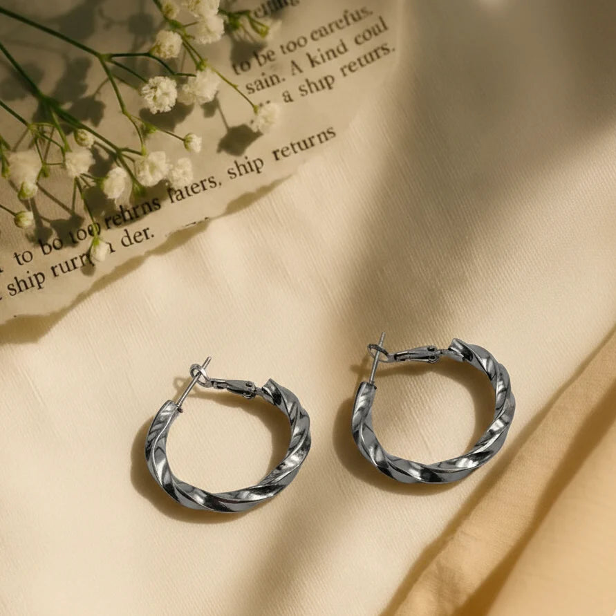 Silver hoop earrings on a beige fabric background with small white flowers.
