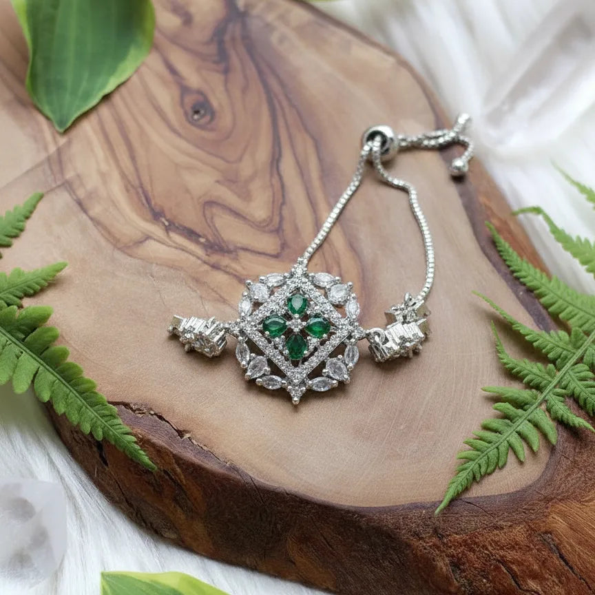 Silver bracelet with green gemstones on a wooden surface with fern leaves