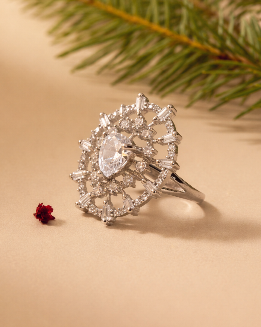Silver ring with a heart-shaped diamond on a beige background with a sprig of greenery.