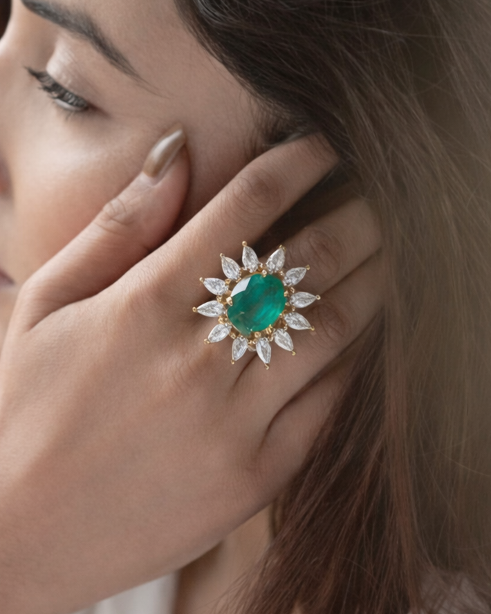 Close-up of a woman's hand wearing an emerald ring with diamond-studded halo.