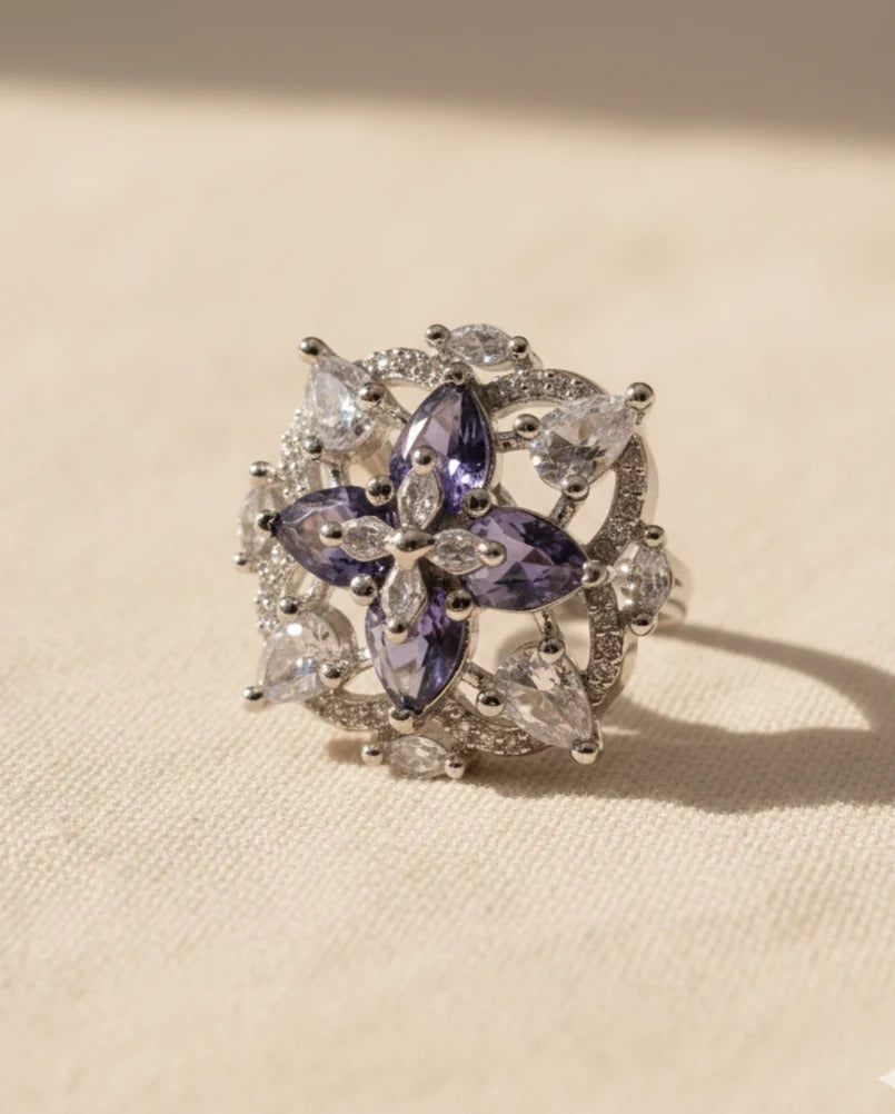 Silver ring with purple and clear gemstones on a beige background