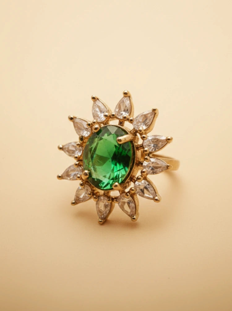 Gold ring with a green gemstone and clear stones on a beige background