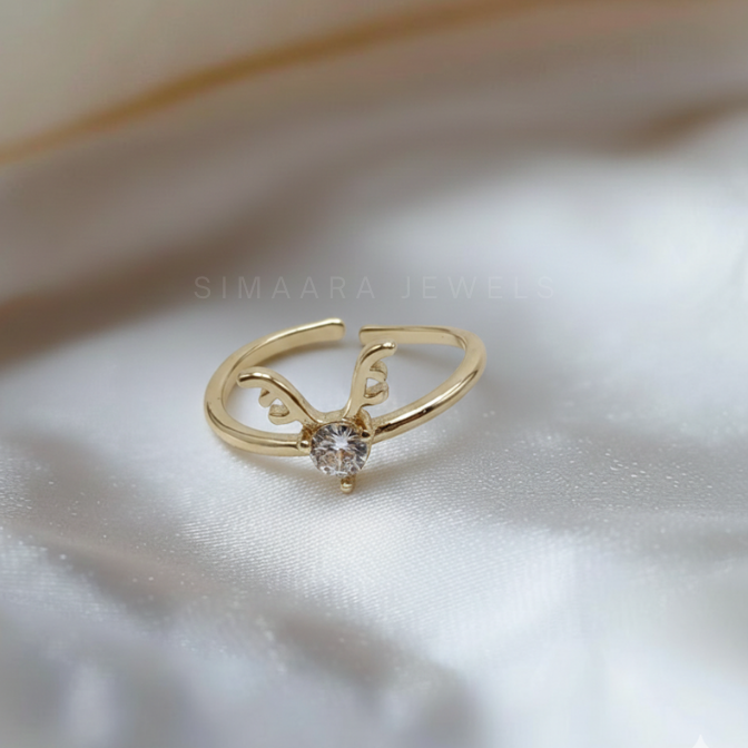 Gold ring with a diamond on a soft white fabric background, featuring the brand 'Simaara Jewels'.