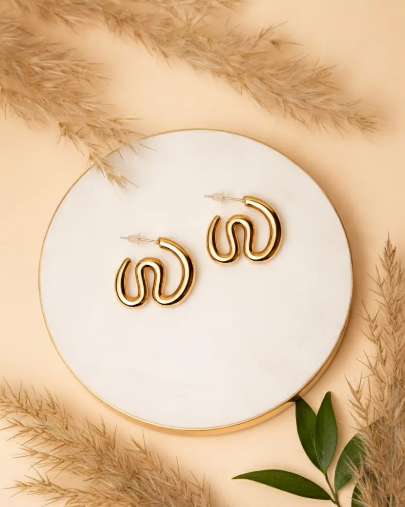 Gold hoop earrings on a white plate with dried grass and leaves around