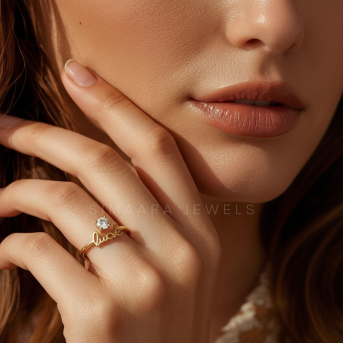 Close-up of a woman's hand wearing a gold ring with a diamond, branded 'Simaara Jewels'.