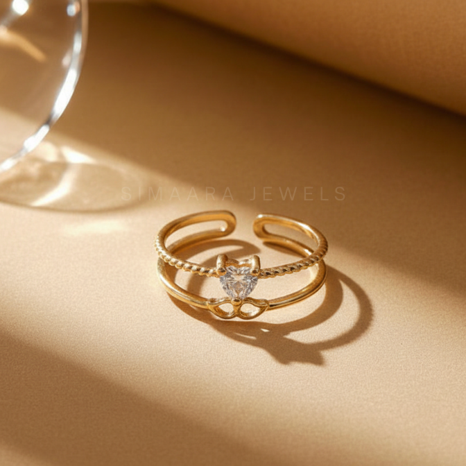 Gold ring with a heart-shaped gemstone on a beige surface, branded 'Simaara Jewels'.