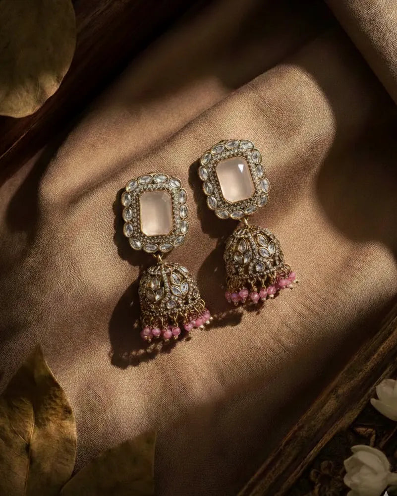 Ornate earrings with pink beads on a textured surface