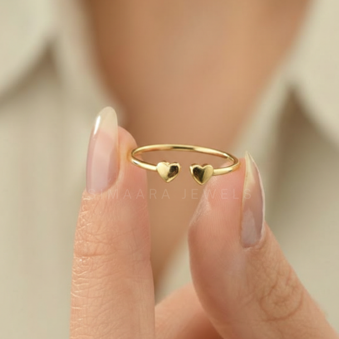 Gold ring with two heart shapes on a finger against a neutral background