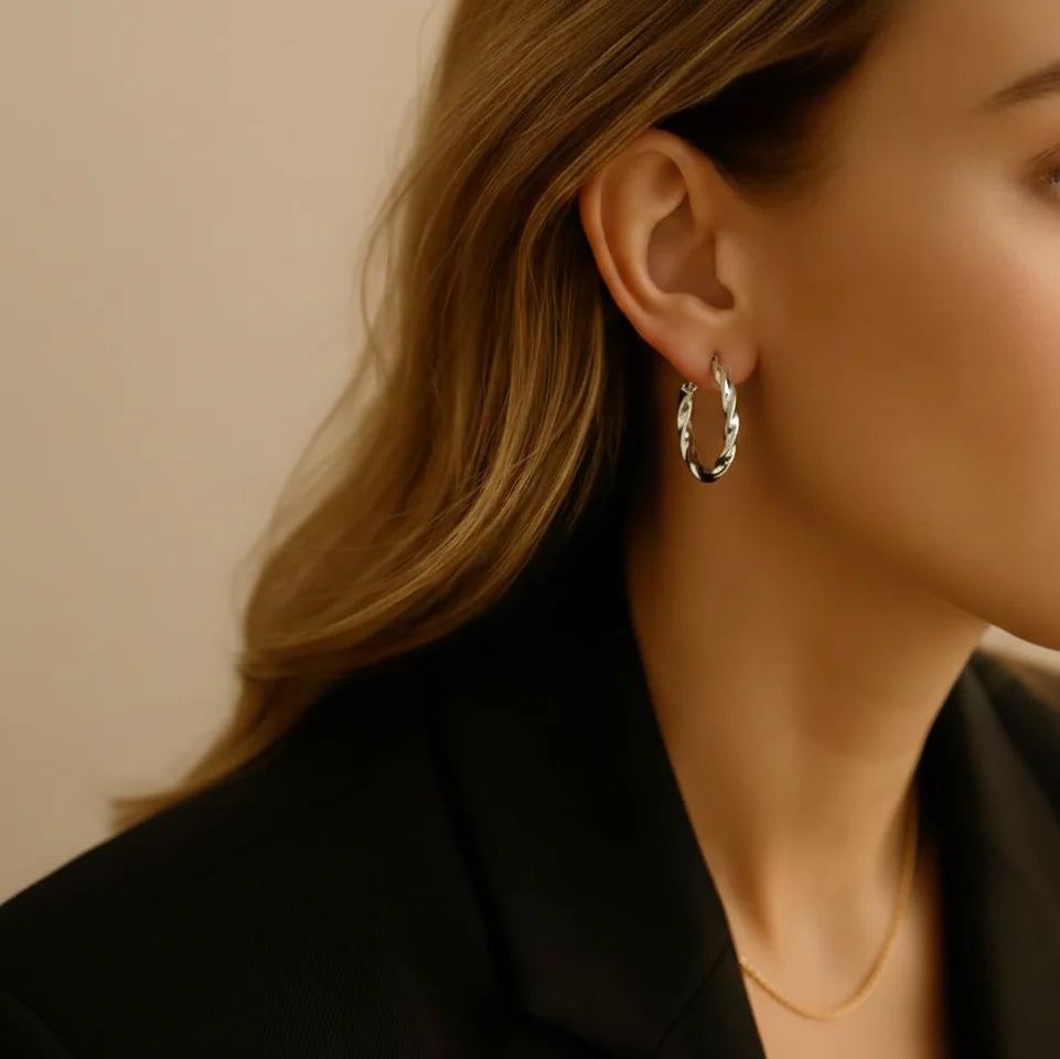 Close-up of a person wearing a silver hoop earring with a neutral background