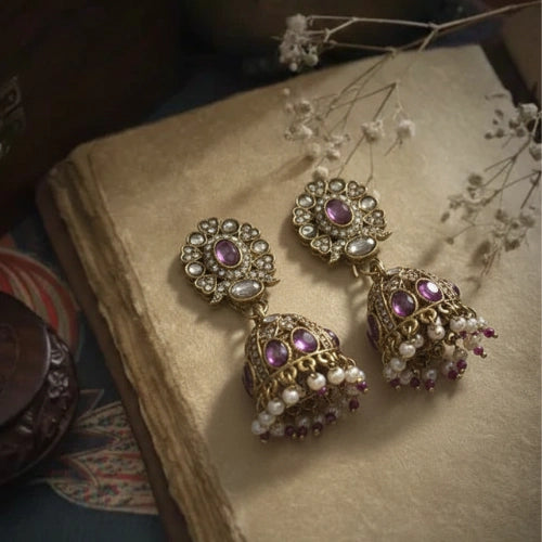 Ornate earrings with purple and pearl accents on an old book