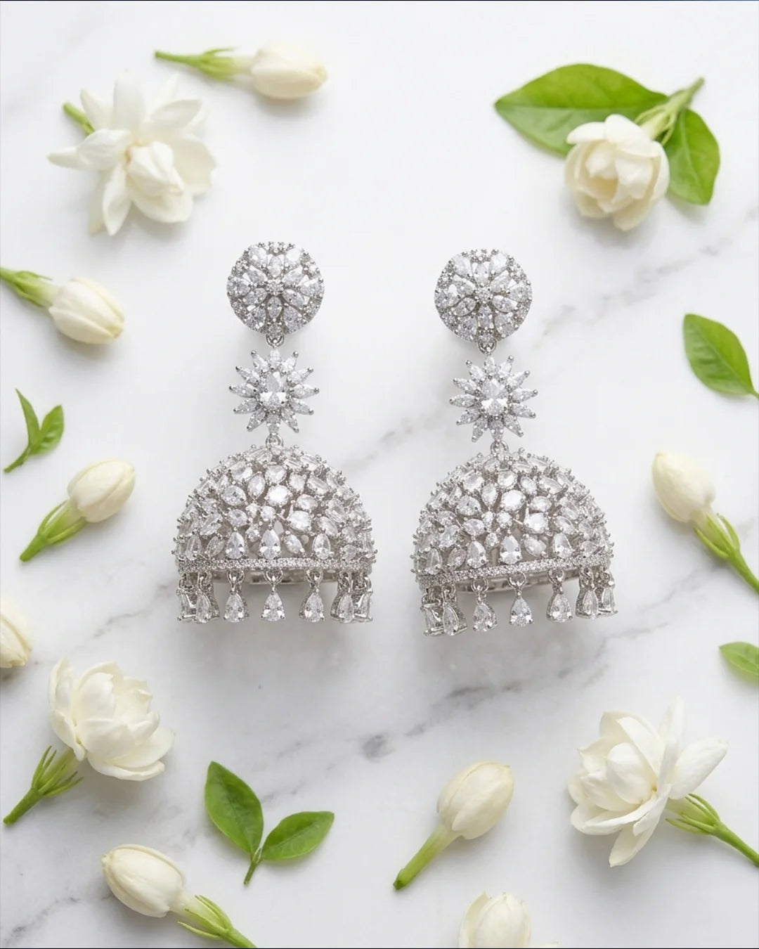Silver earrings with floral design on a marble surface with white flowers and green leaves.