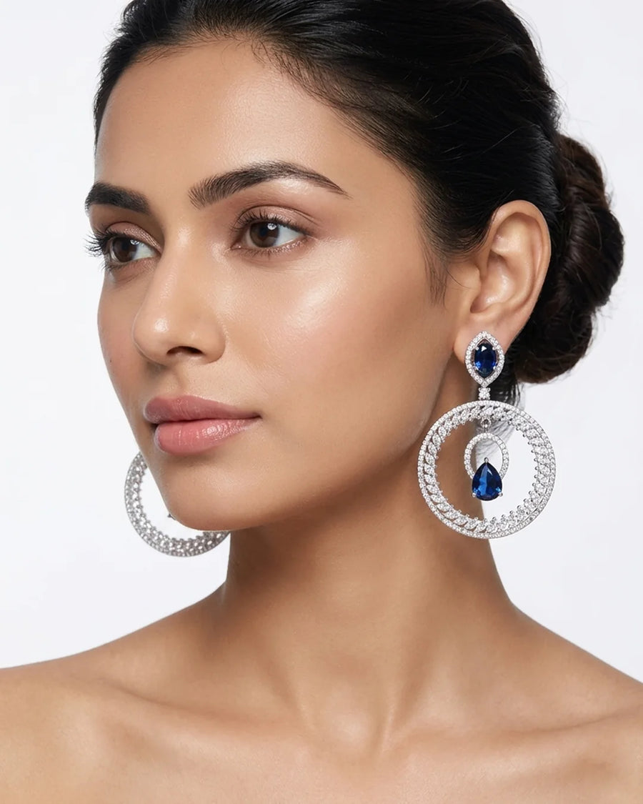 Woman wearing silver hoop earrings with blue gemstones on a white background