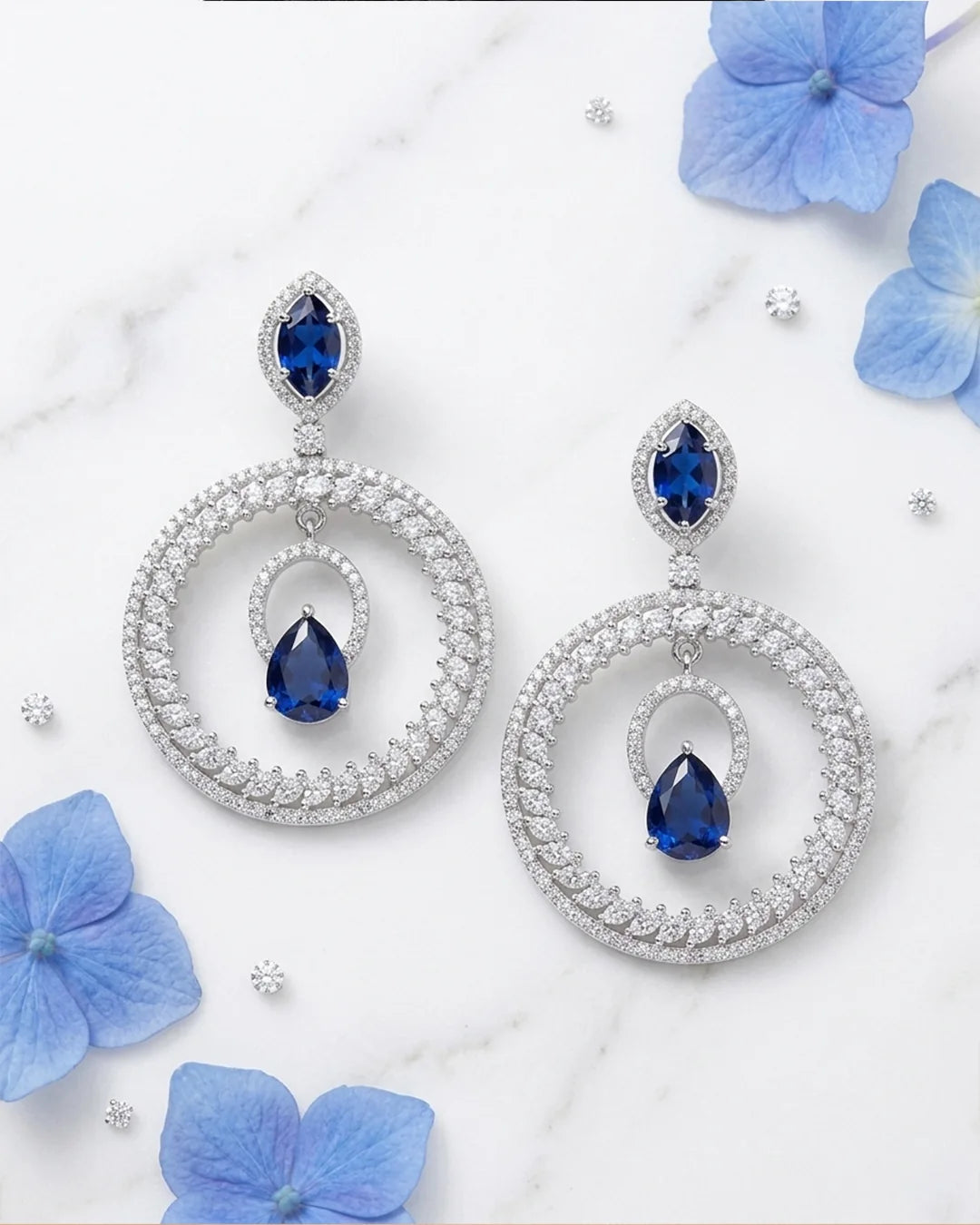 Pair of silver earrings with blue gemstones on a white surface with blue flowers.