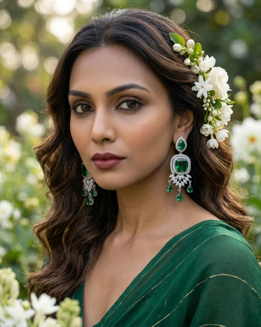Woman in a green saree with floral hair accessories and earrings, standing in a garden.