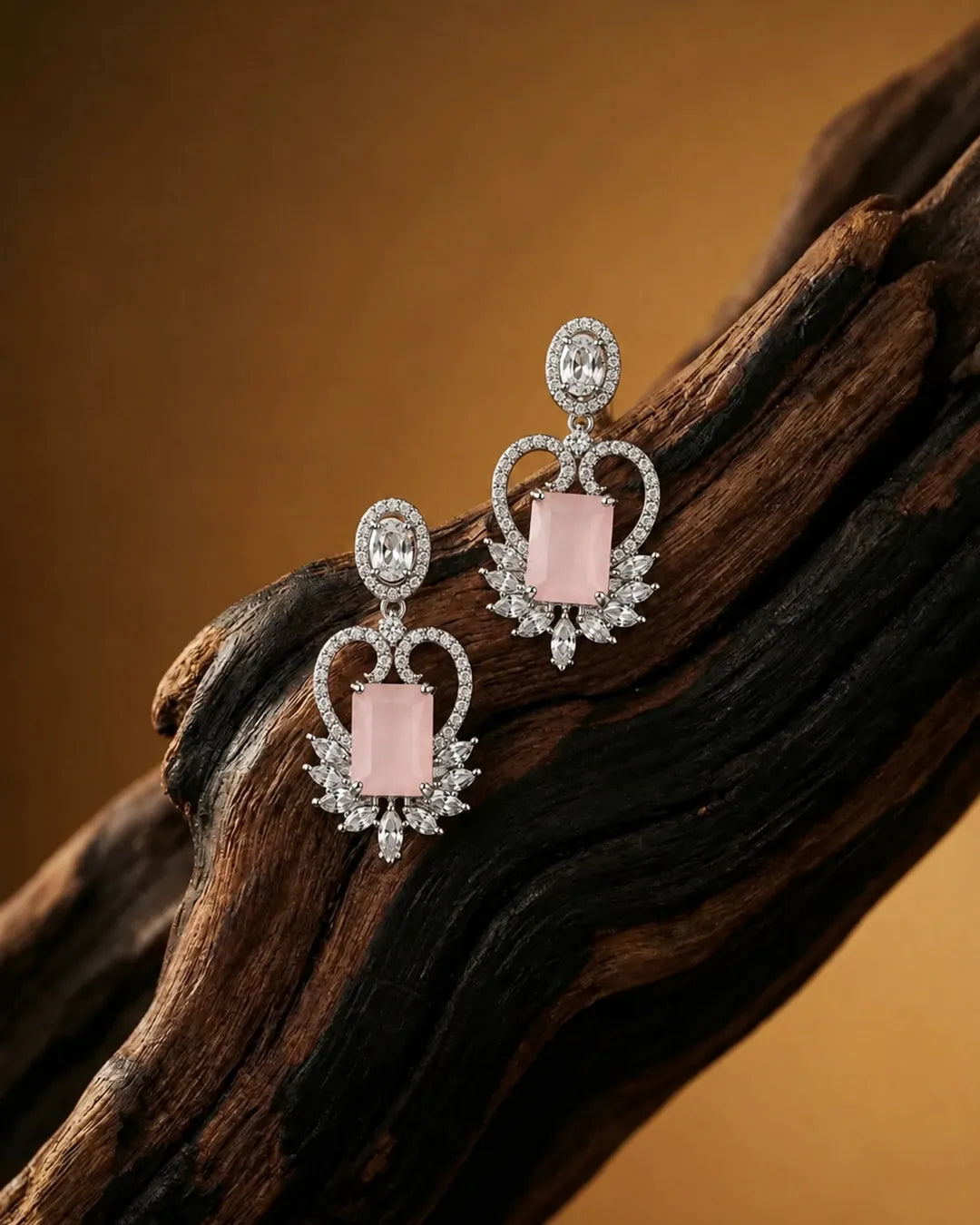 Pair of earrings with pink stones and diamond-like elements on a wooden surface.