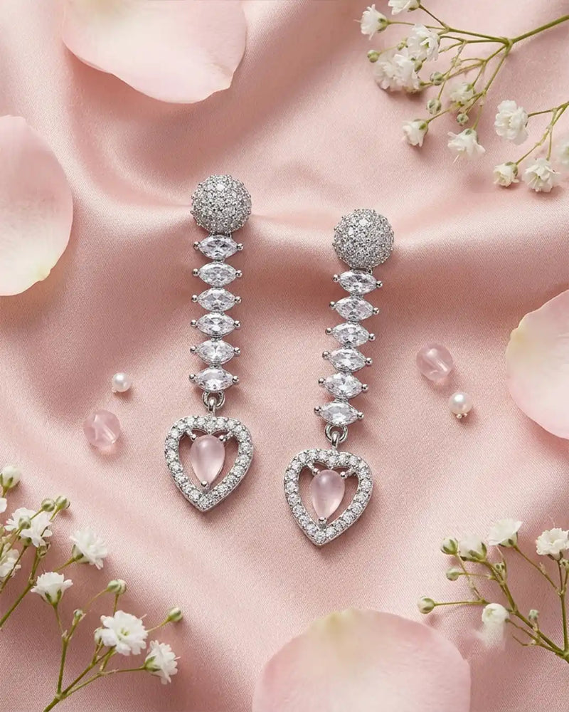 Diamond earrings with heart-shaped pink gemstones on a soft pink background with flowers.