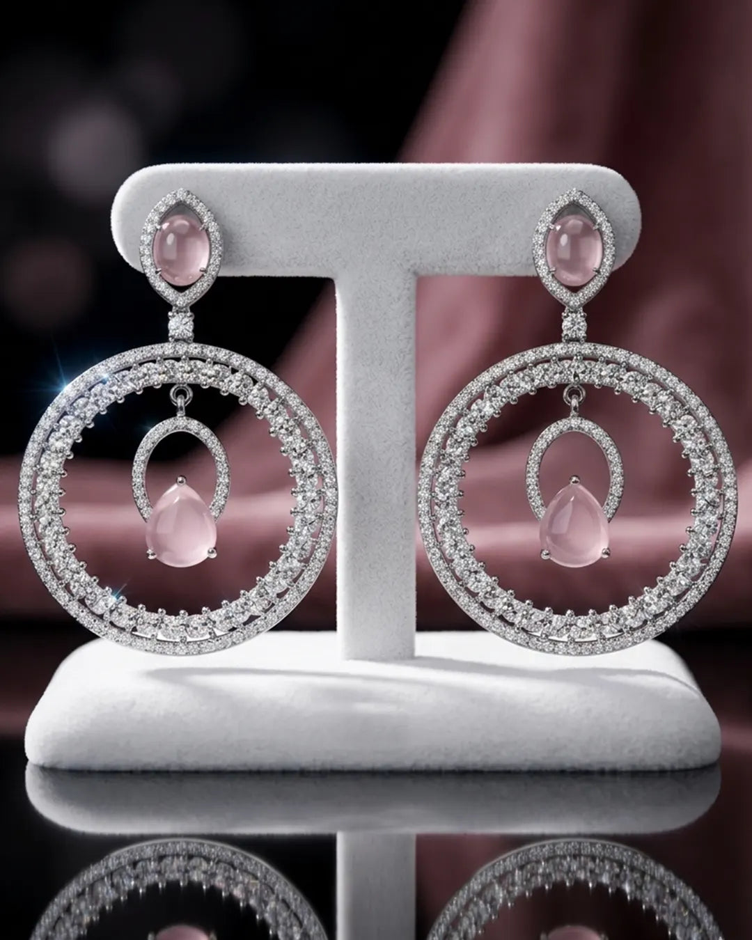Pair of silver earrings with pink gemstones on a white stand against a dark background