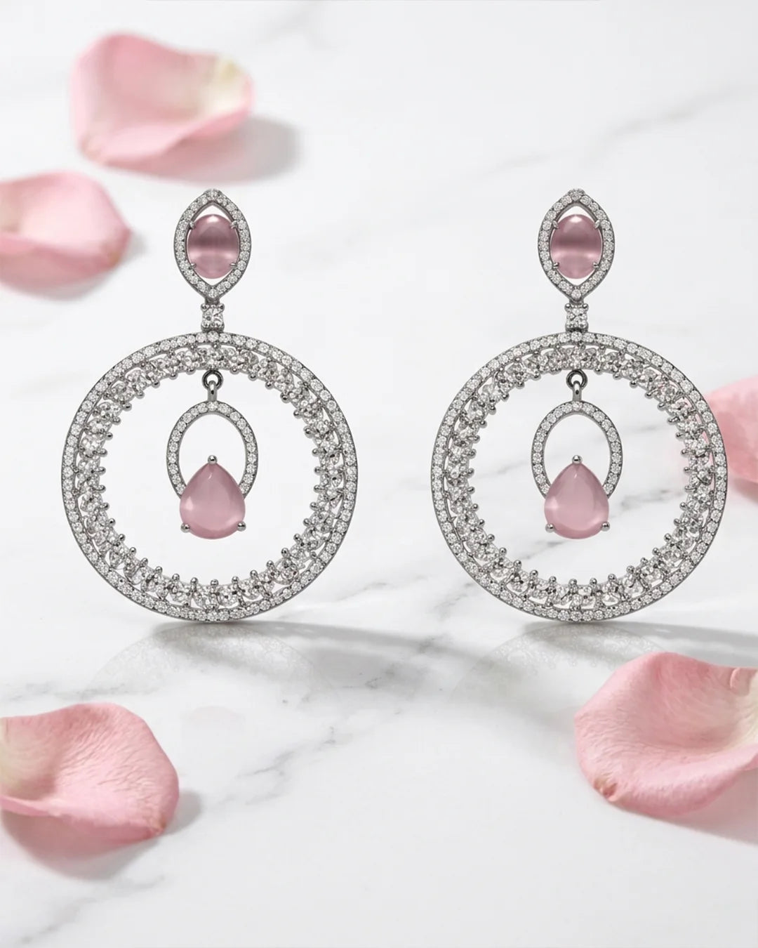Pair of silver earrings with pink gemstones on a marble surface with pink petals.