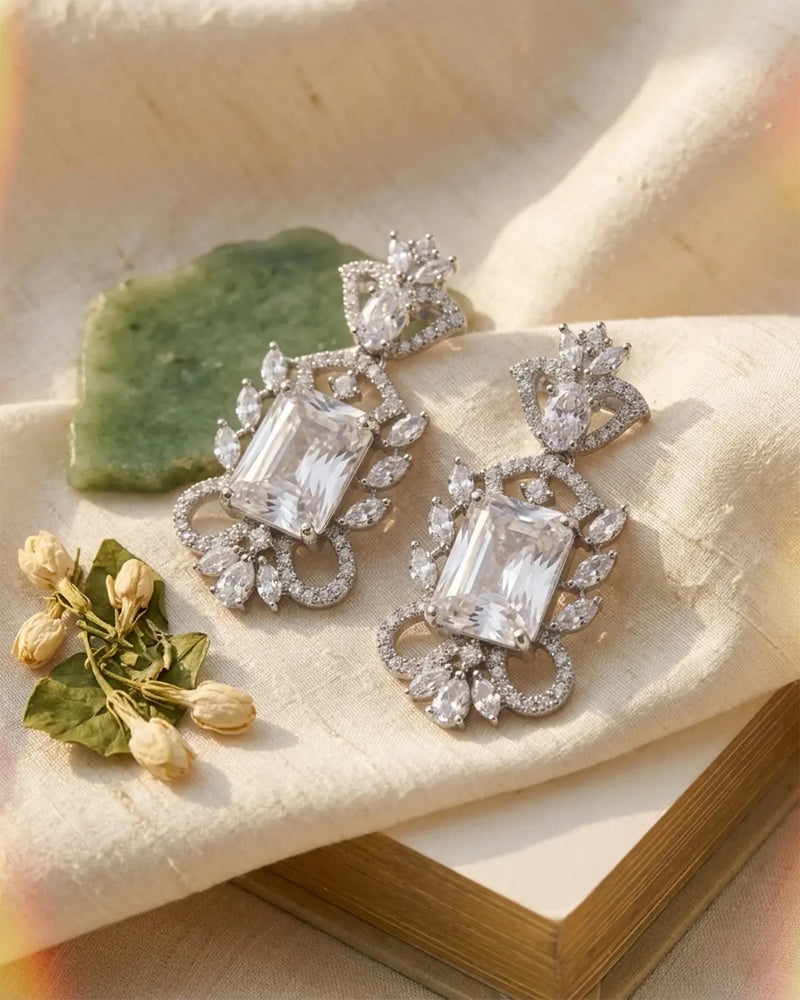 Pair of diamond earrings on a textured surface with green leaves and flowers.
